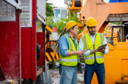 two men in safety gear are looking at a piece of machine